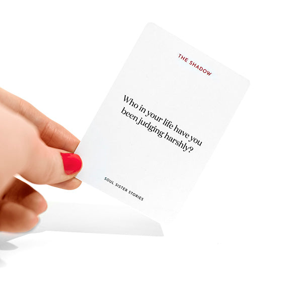 Hand holding a card. Text on card says Who in your life have you been judging harshly?